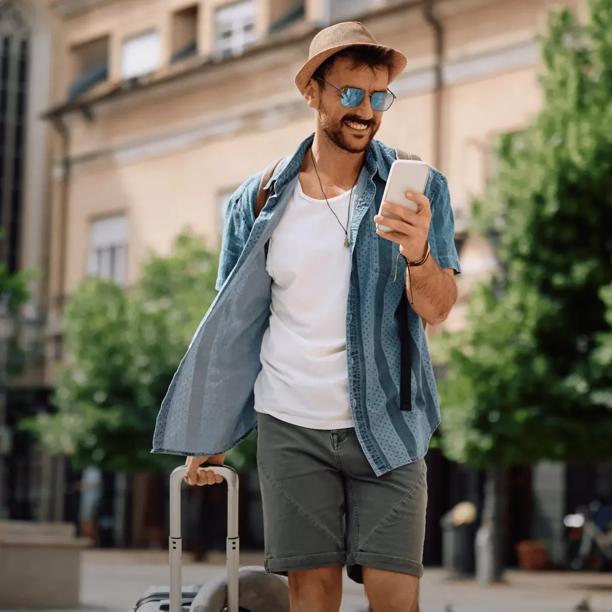Man with suitcase smiling at phone outdoors.